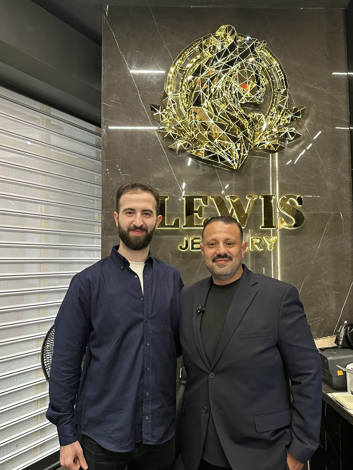 Two colleagues in front of the Lewis Jewelry brand wall inside the new branch.