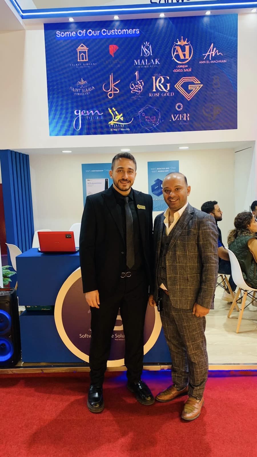 Two colleagues beneath the stand's customer wall at NEBU Expo 2023.